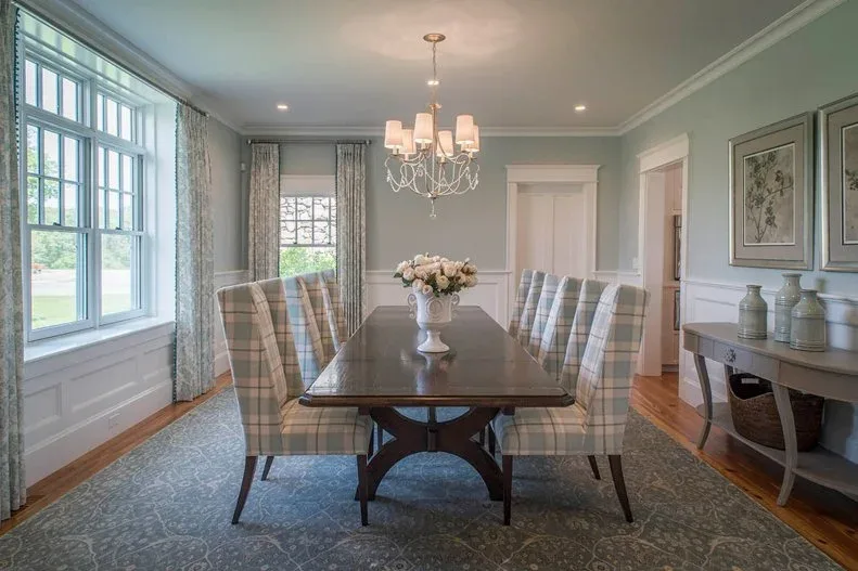 Dark wooden dining table with plaid high-backed chairs, pale blue walls and a white shaded chandelier.