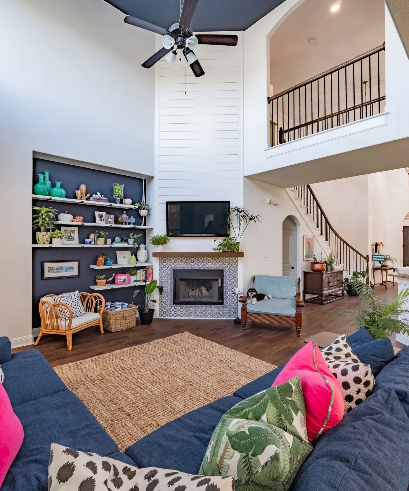 Tall white paneled fireplace beside dark display shelves, blue seating and an upper gallery.