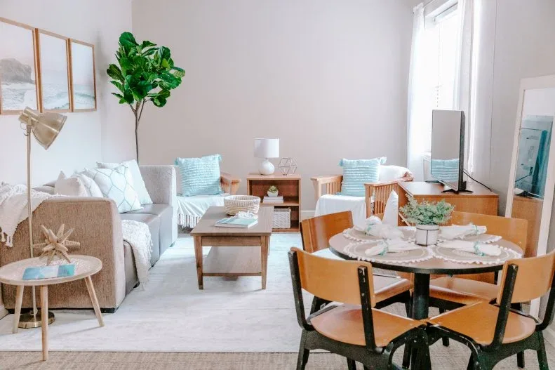 Student shared lounge with gray sofa, wooden armchairs, pale blue cushions, low coffee table and compact dining table.