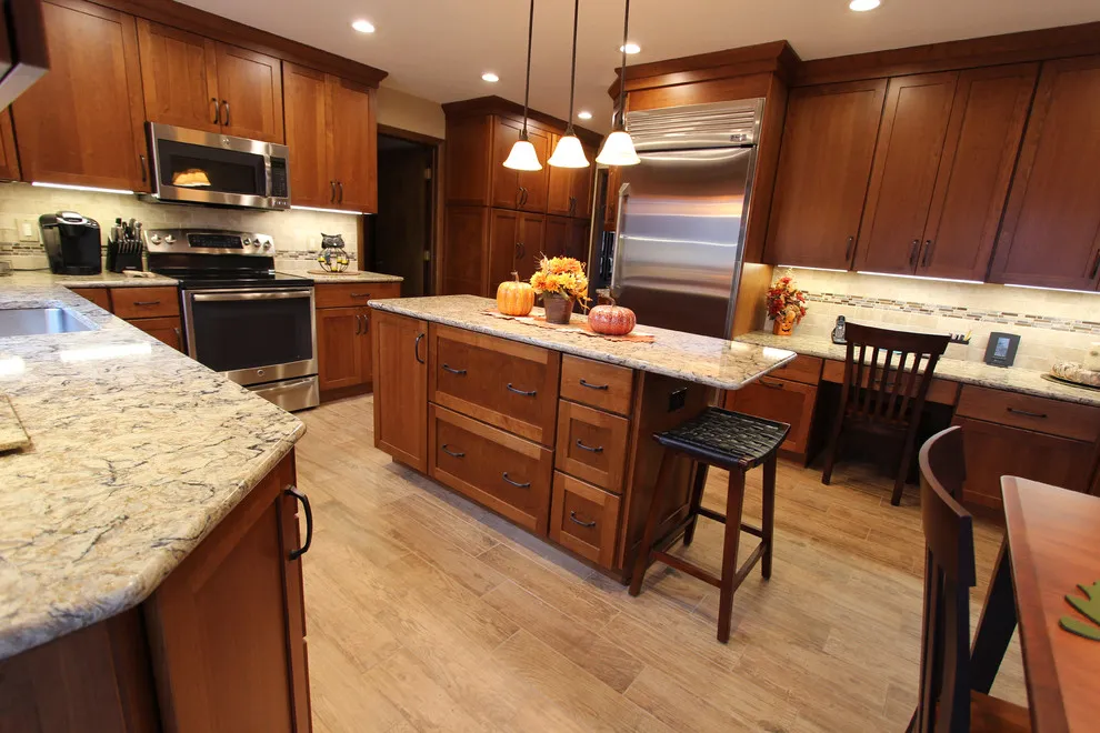 Warm wood cabinets sit below pale counters in a kitchen with an island and dark chairs
