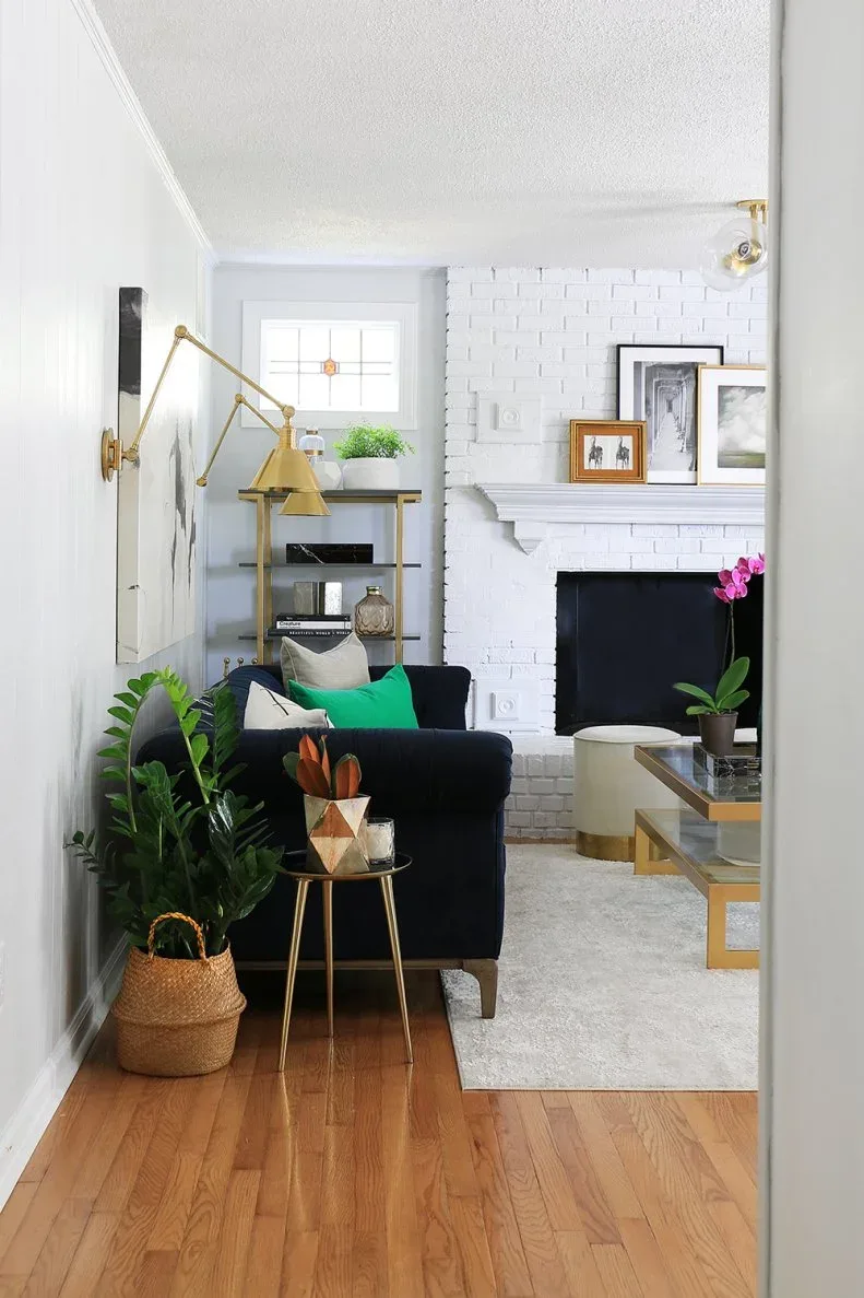 White brick fireplace with white mantel, layered black, white and wood-toned frames and gold-toned lighting