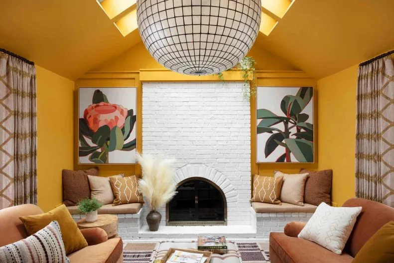 White brick arched fireplace centered in yellow room with two large floral pictures, benches and warm seating