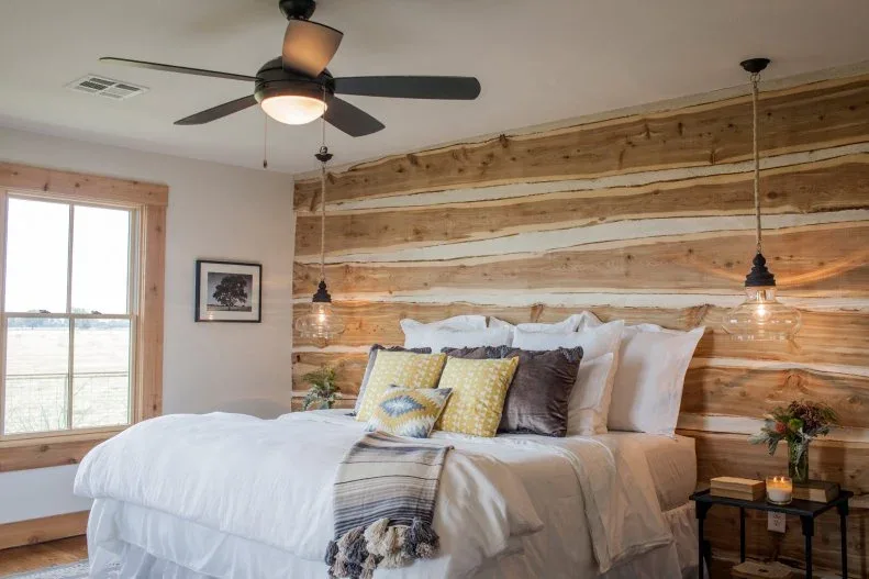 Varied warm wood boards behind pale bedding with yellow cushions and hanging bedside lights