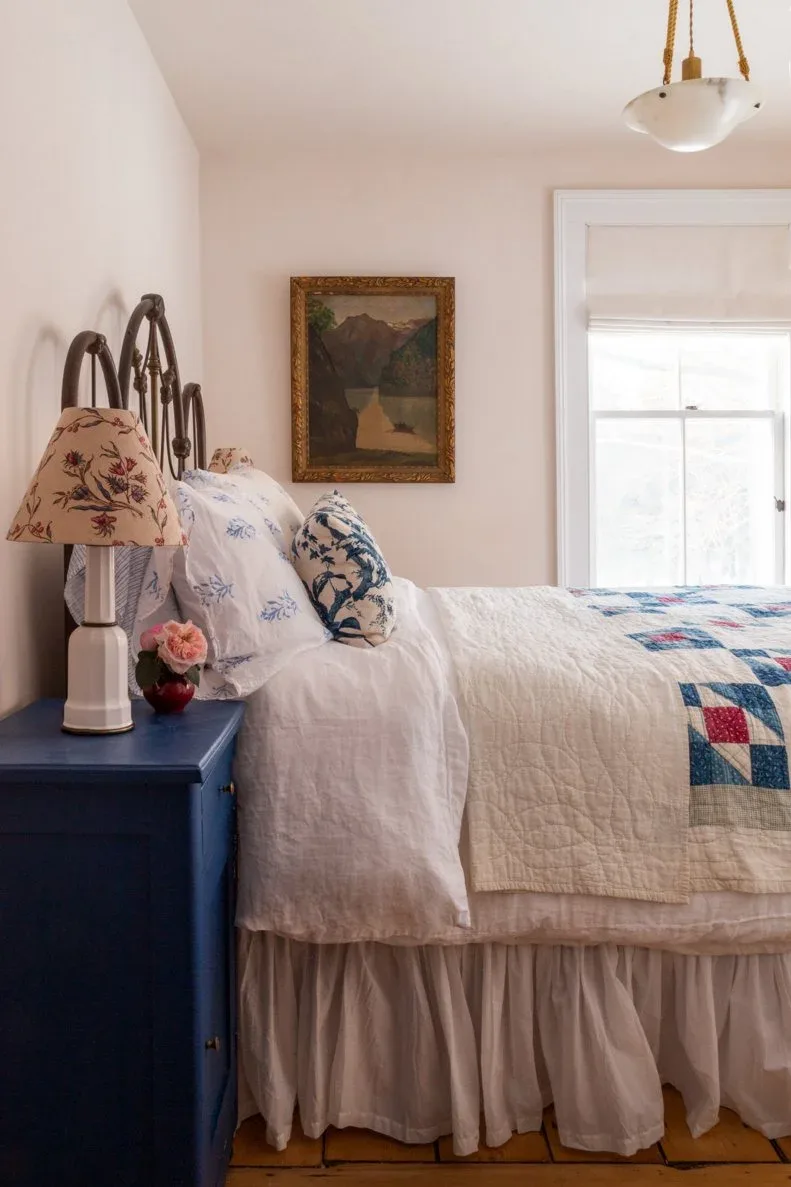 Country bedroom with dark curved metal bed, blue chest, floral lamp shade and patchwork quilt