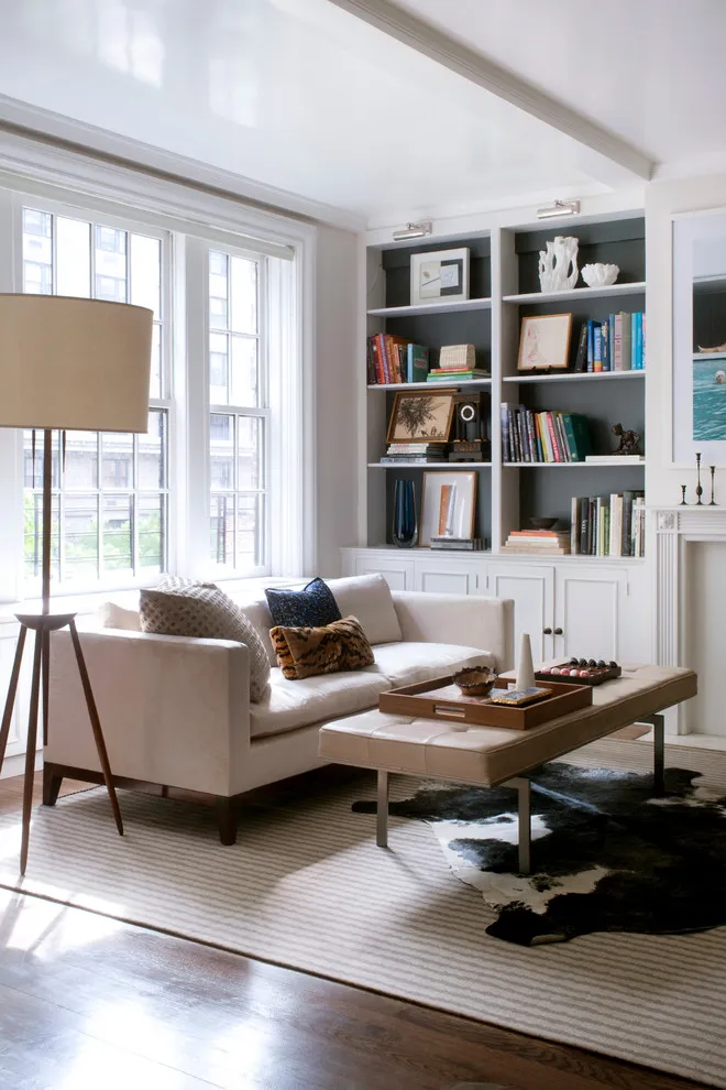 A small beige sofa sits beside a slim table and built-in shelves near a large window