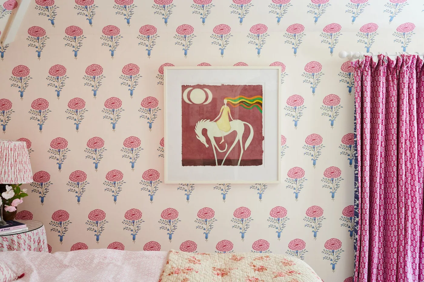 Rows of stylized pink flowers on cream wallpaper behind a bed and a framed horse picture.