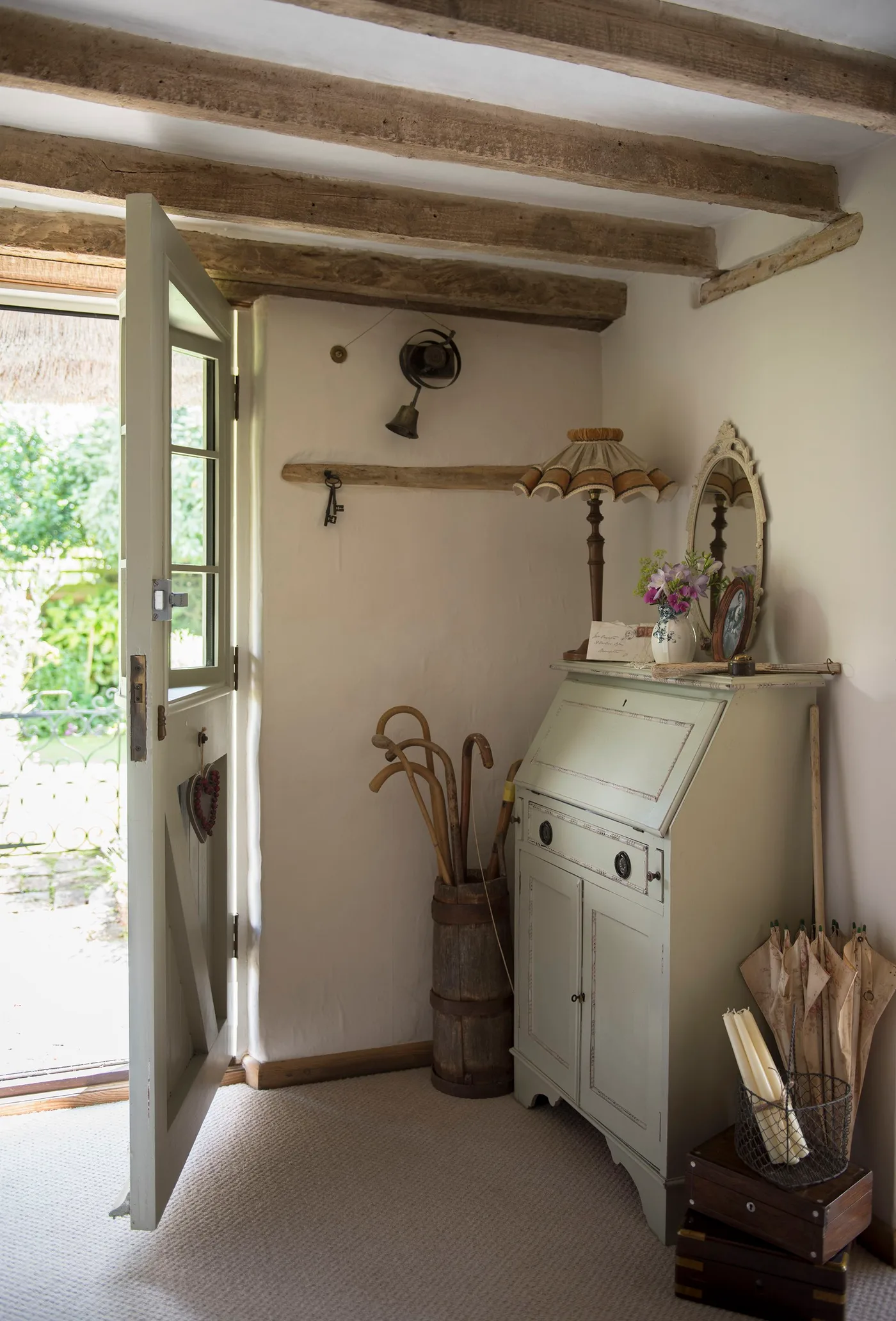 Small entrance with an open pale green door, exposed beams, painted writing cabinet, decorative mirror and umbrella containers.