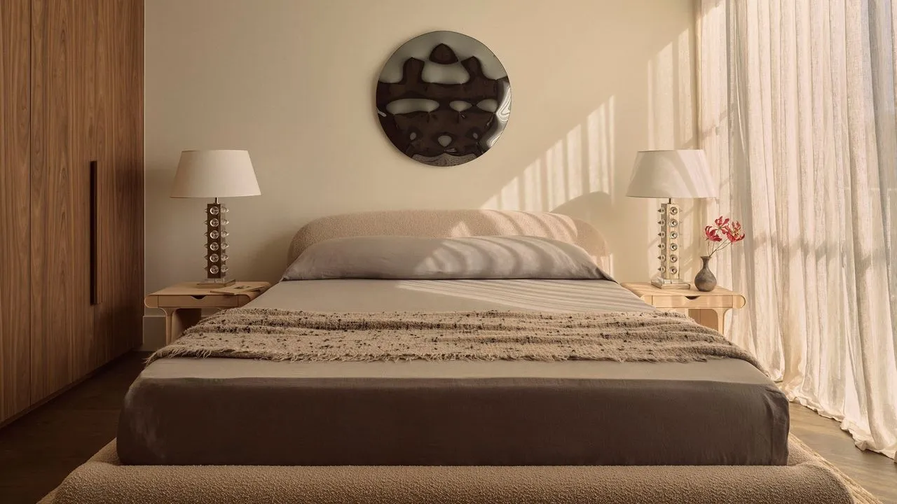 Light curtains frame a bed with quiet textured bedding and small bedside lamps.