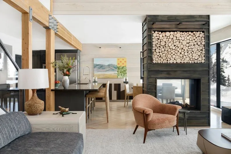 A straight dark fireplace partition with a glass-sided opening and upper log display stands between living and dining areas beside a pink chair