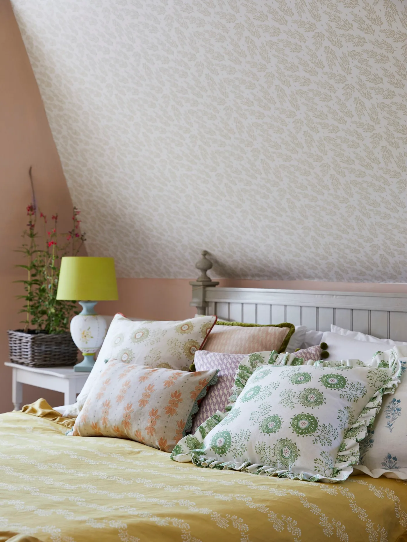 Bedroom detail with pale patterned sloped ceiling, pink wall, gray headboard and green-accented cushions