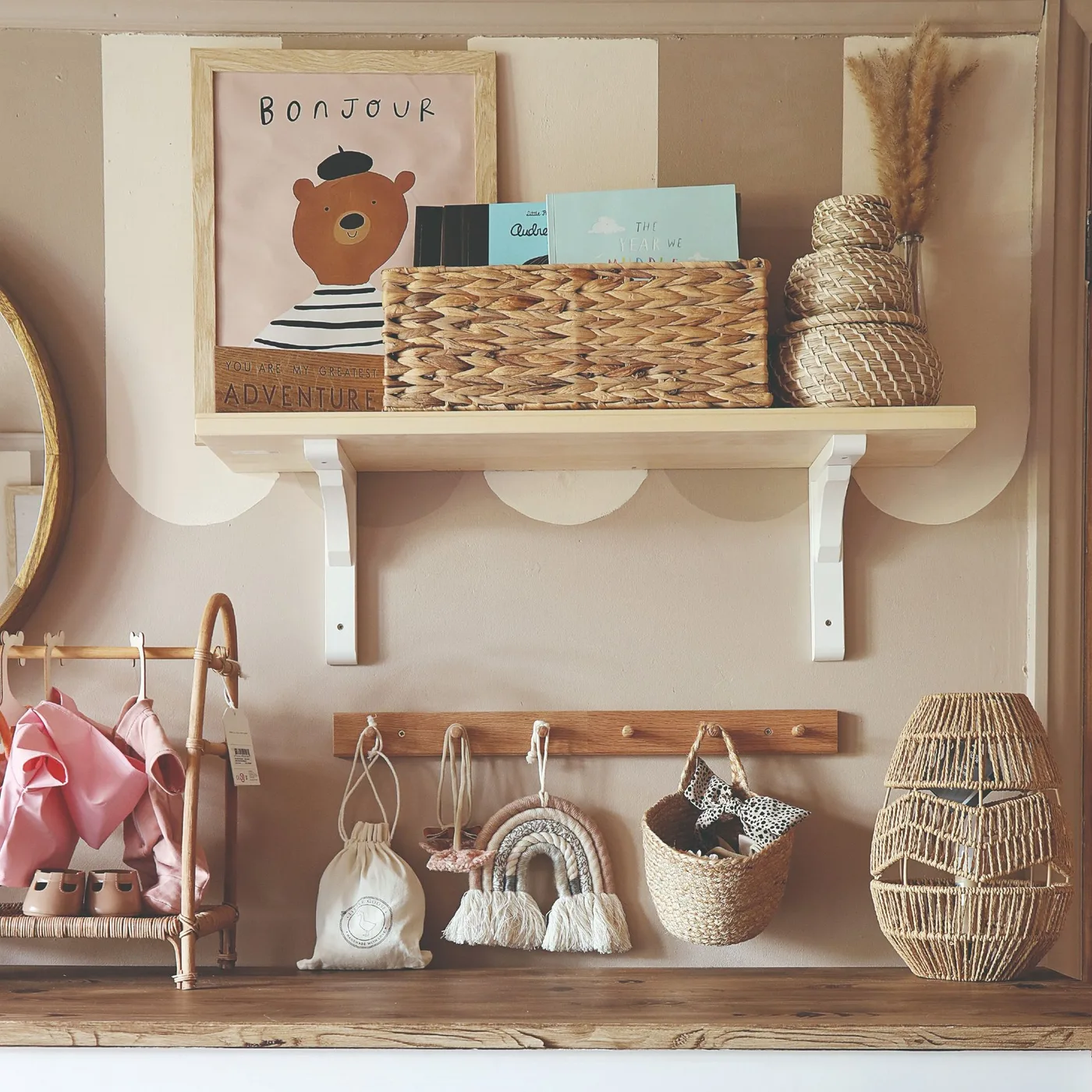 Soft scalloped wall edge around pale shelf and warm peg rail with woven baskets and selected nursery objects.
