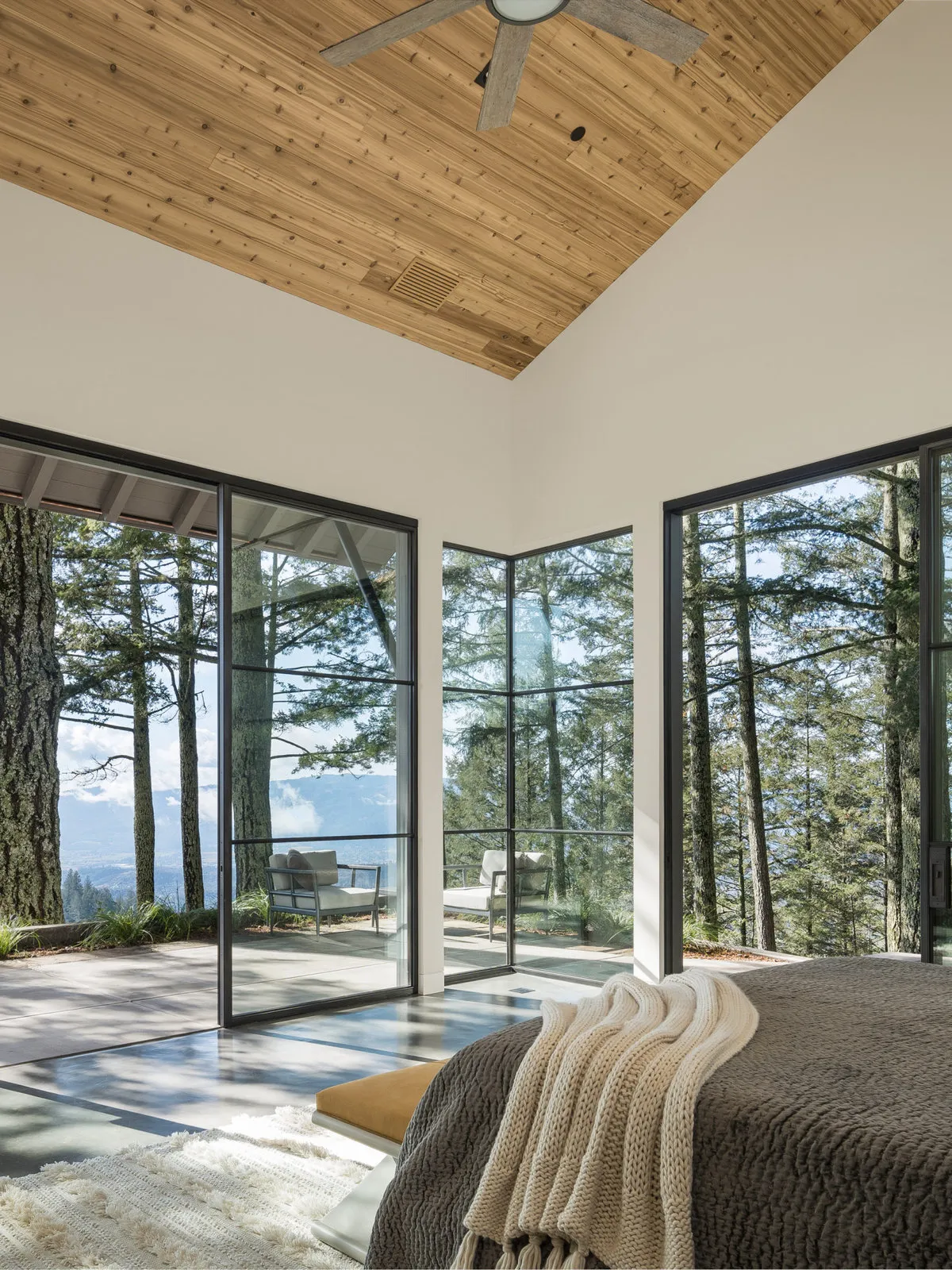 A low bed sits near broad windows beneath a pitched timber ceiling.