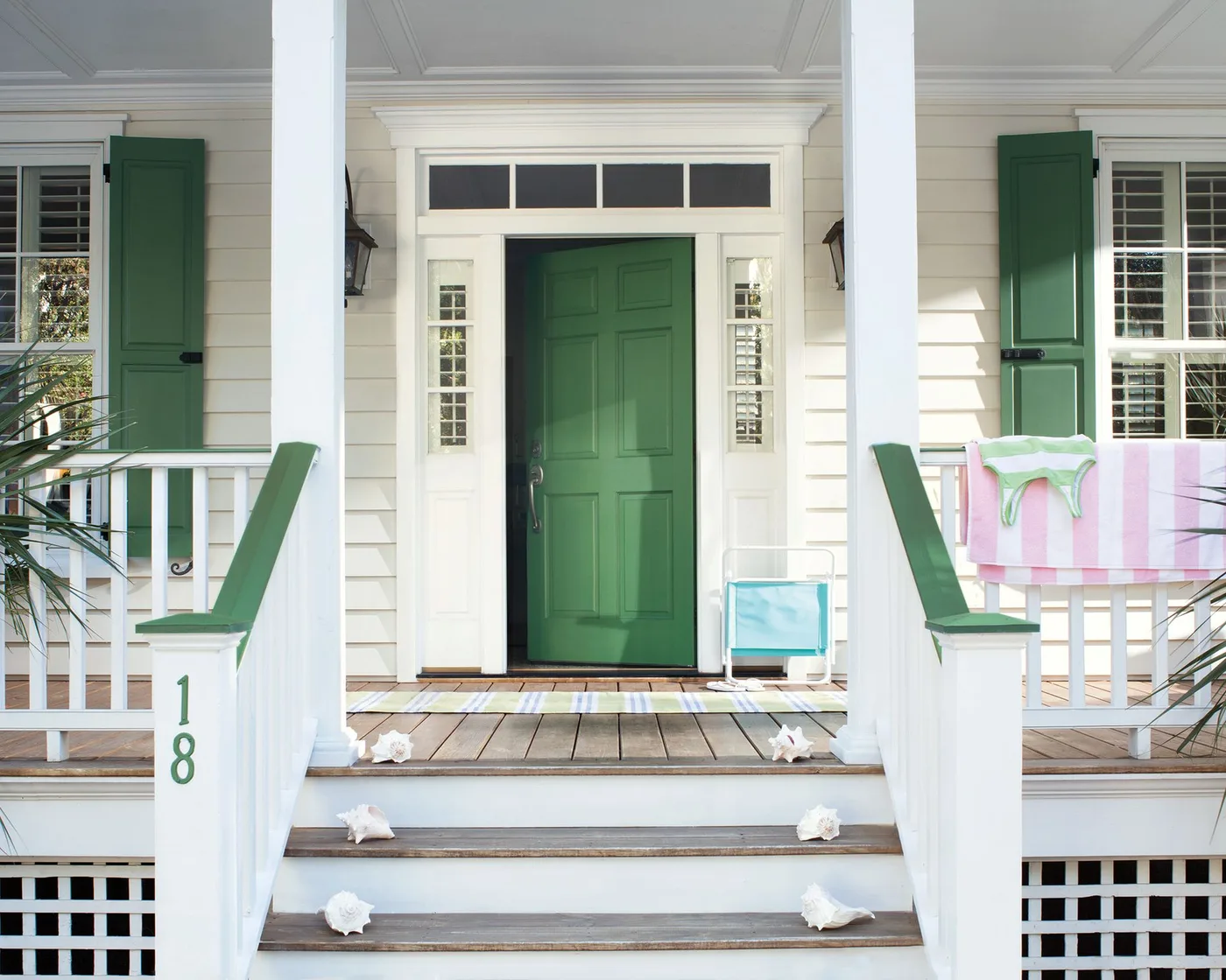 White country porch with green door and shutters, wood deck, pale rails and striped outdoor textiles