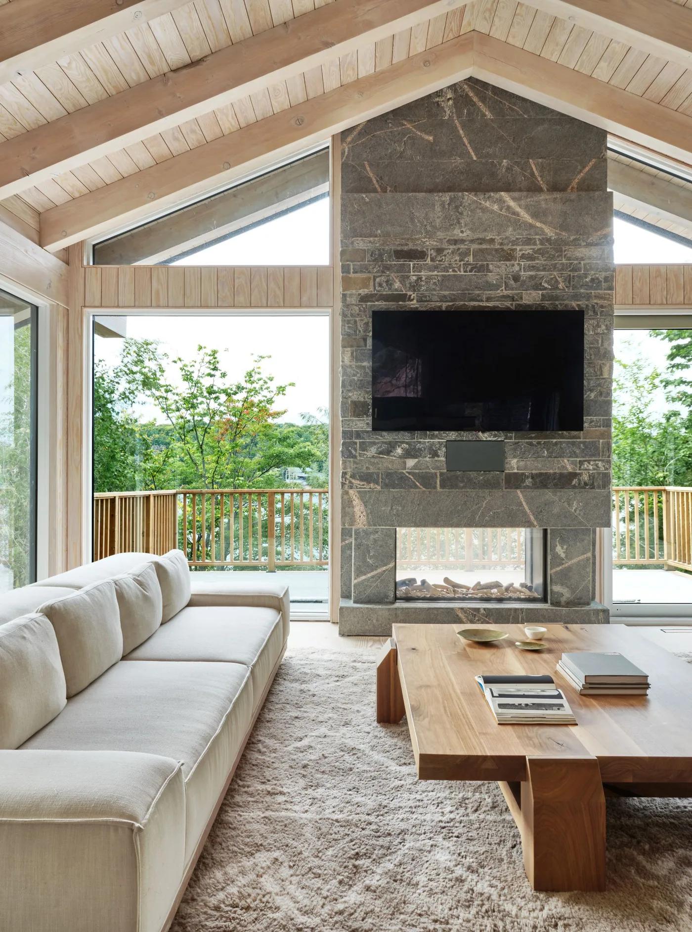 Tall gray veined fireplace wall beneath pitched wood ceiling with television, glazed opening and large windows