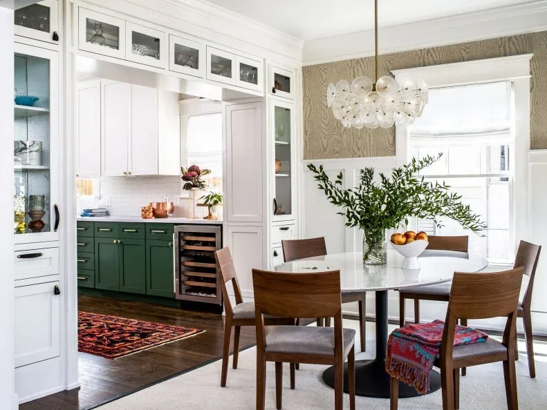 White glazed dining cabinets around an opening with green lower cabinets and bottle storage behind a round table