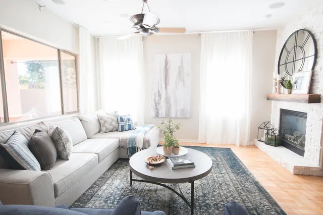 A pale corner sofa sits above a blue patterned rug near bright windows.
