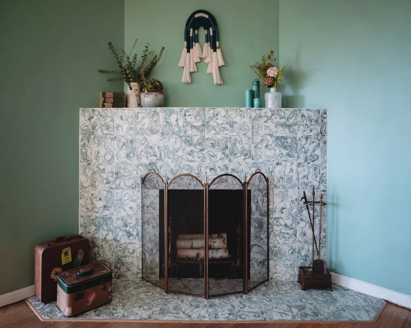 Patterned pale fireplace and hearth in a green corner with a folding screen and decorative objects.