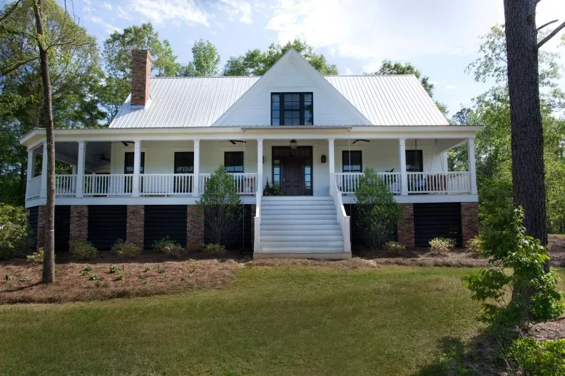 White farmhouse with broad raised wraparound porch, central steps and simple white railing