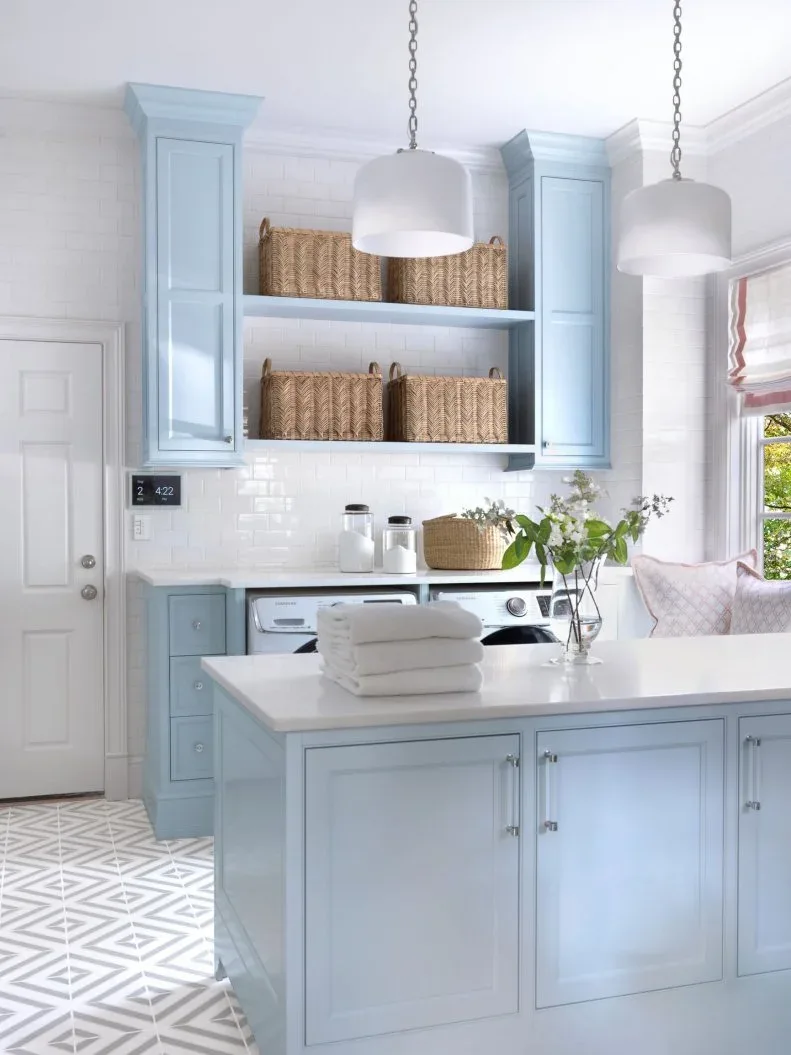Pale blue laundry cupboards and island with open basket shelves, white pendant shades, patterned floor and side-by-side appliances