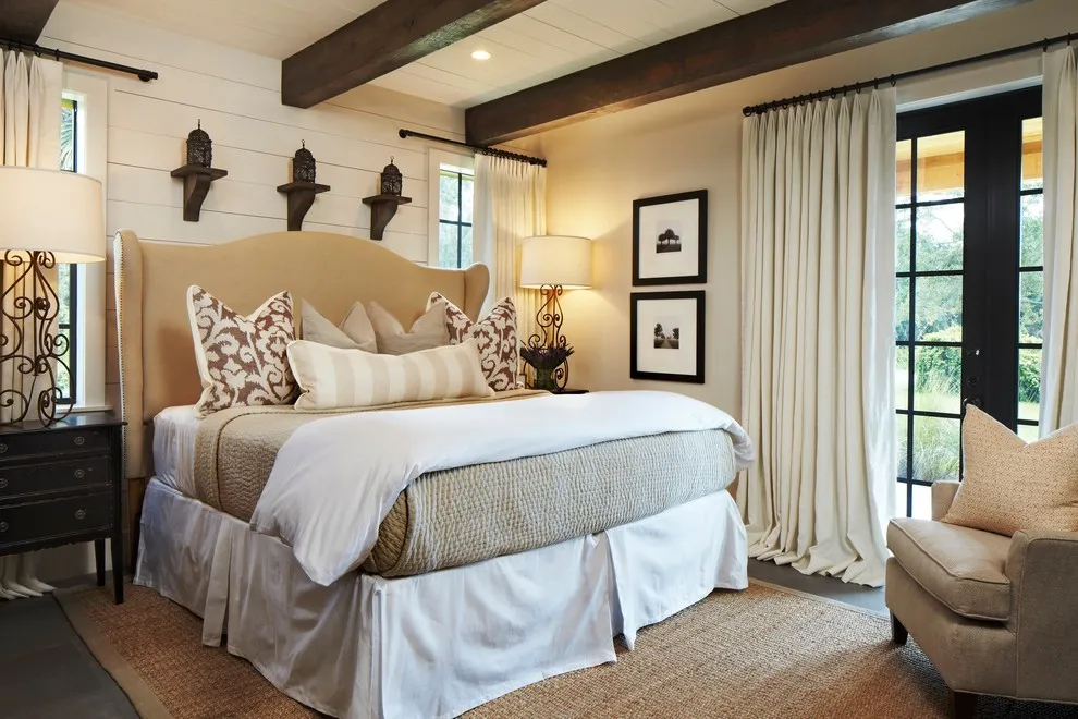 A beige bed stands beside dark-framed art and timber ceiling accents