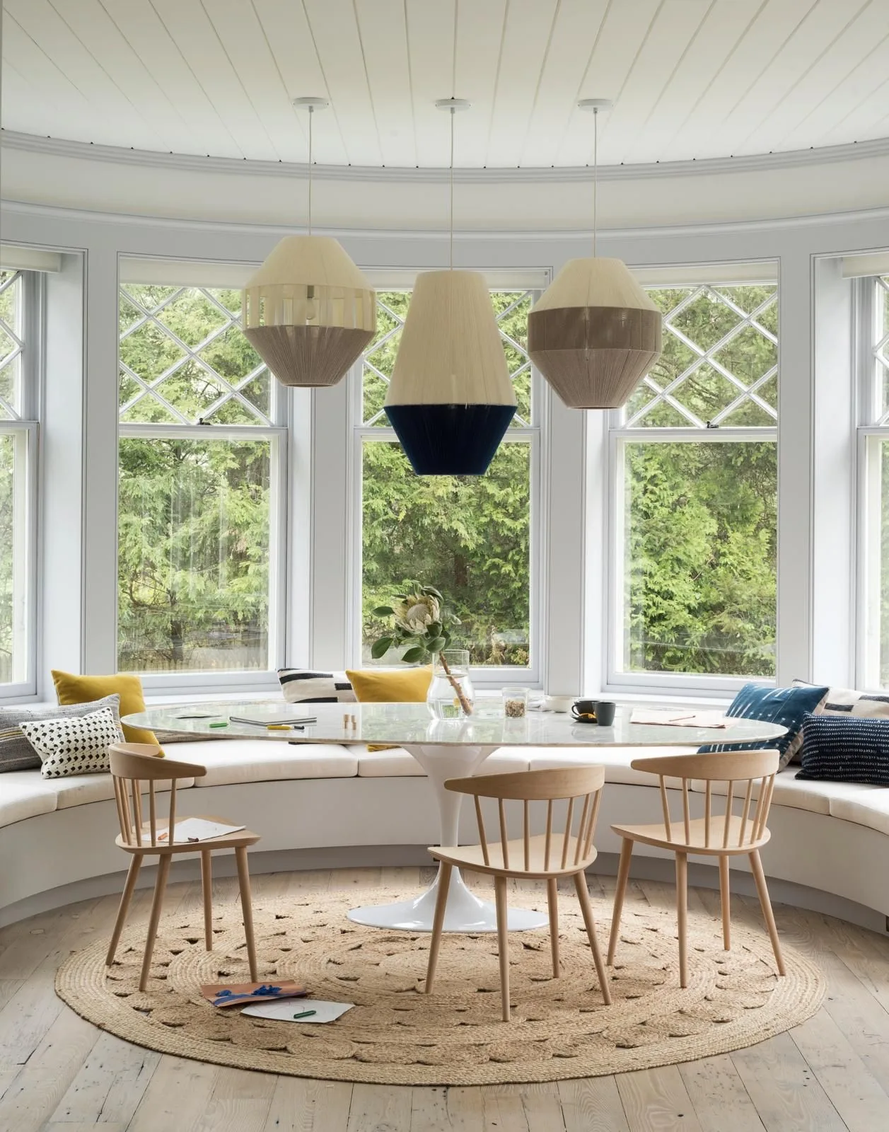 Three pale geometric pendants above a round dining table within a curved window bench