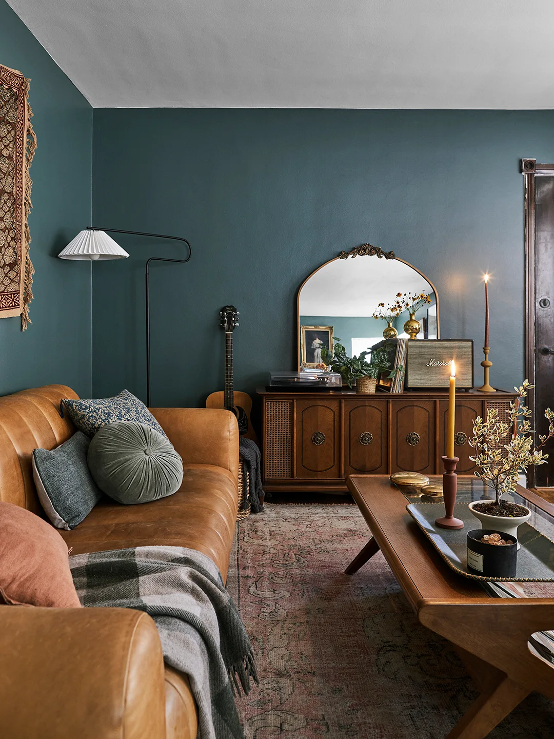 Brown couch with green gathered round pillow, darker square pillows and a checked throw beside blue walls.