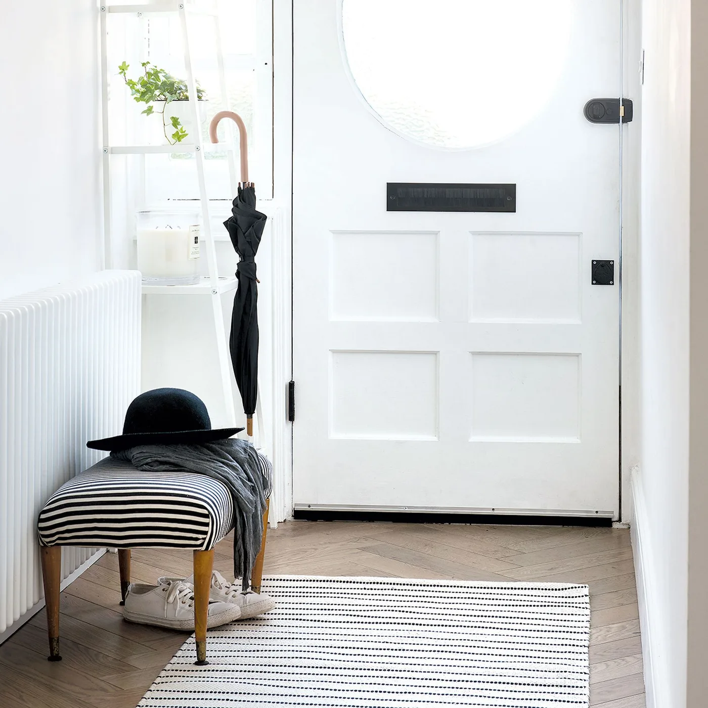 Small black and white striped rug beneath a striped upholstered stool beside a white front door and radiator