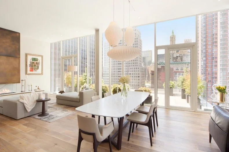 Cluster of pale rounded pendants above a white dining table beside tall windows in an open living area