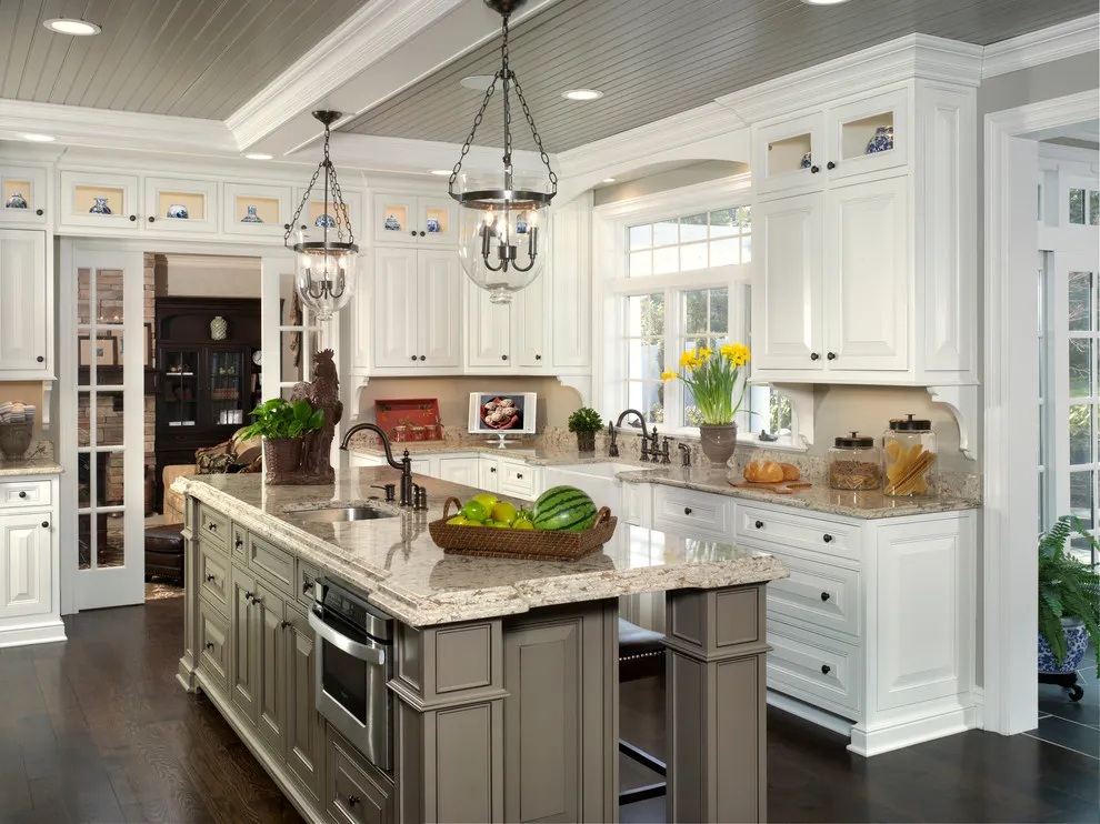 White upper cabinets with decorative glass sit above a darker taupe island in a traditional kitchen
