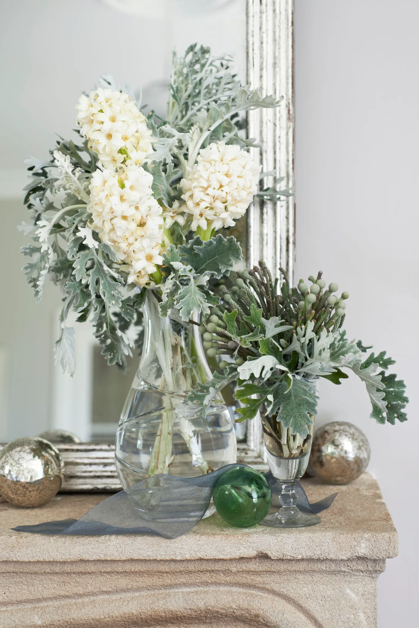 Pale textured mantel with reflective mirror, cream flowers, silvery green foliage and small decorative spheres