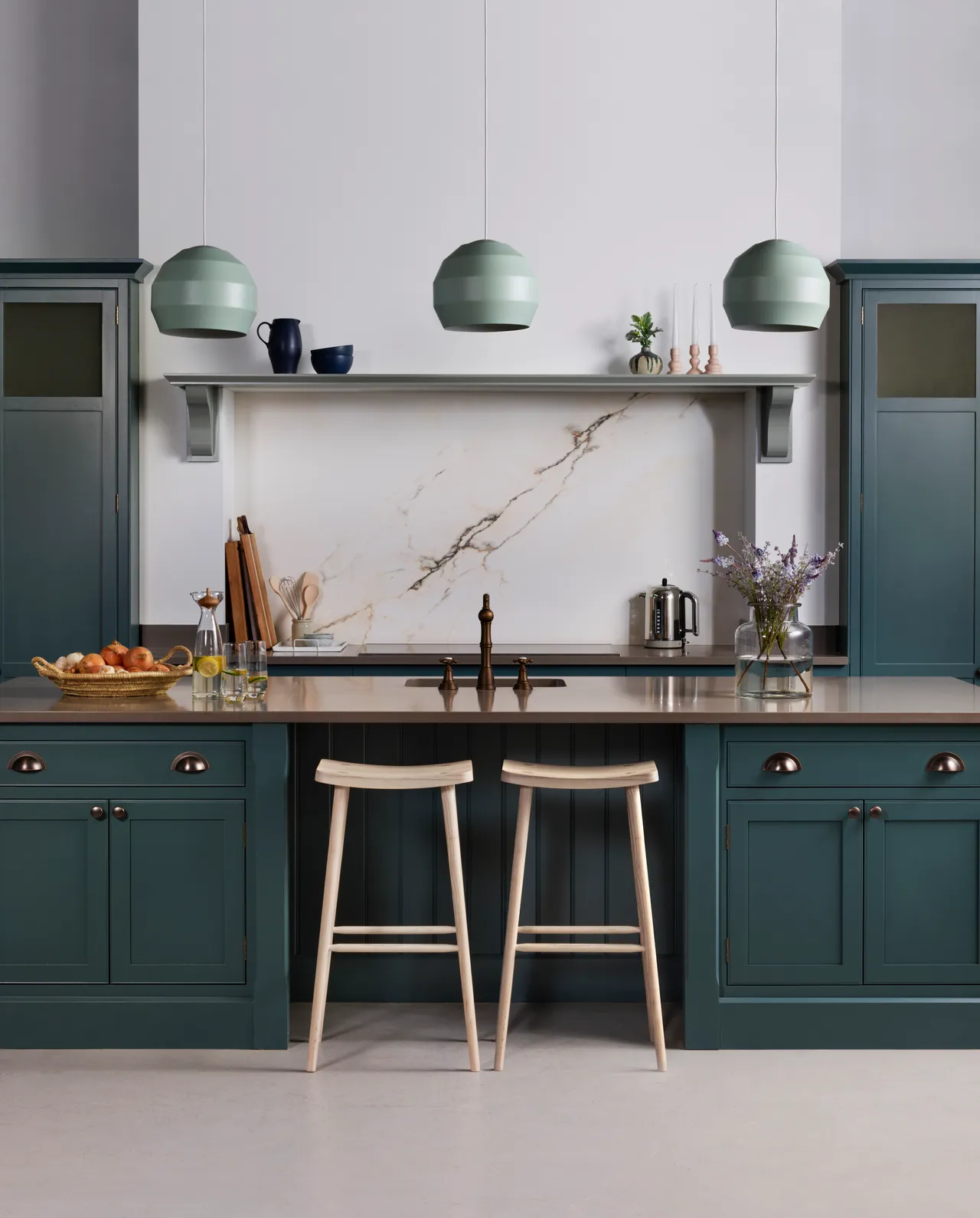Deep green lower cabinets sit below a pale stone backsplash and open shelf