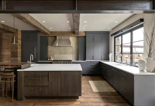 Charcoal perimeter cabinets wrap around a timber island beneath exposed beams.