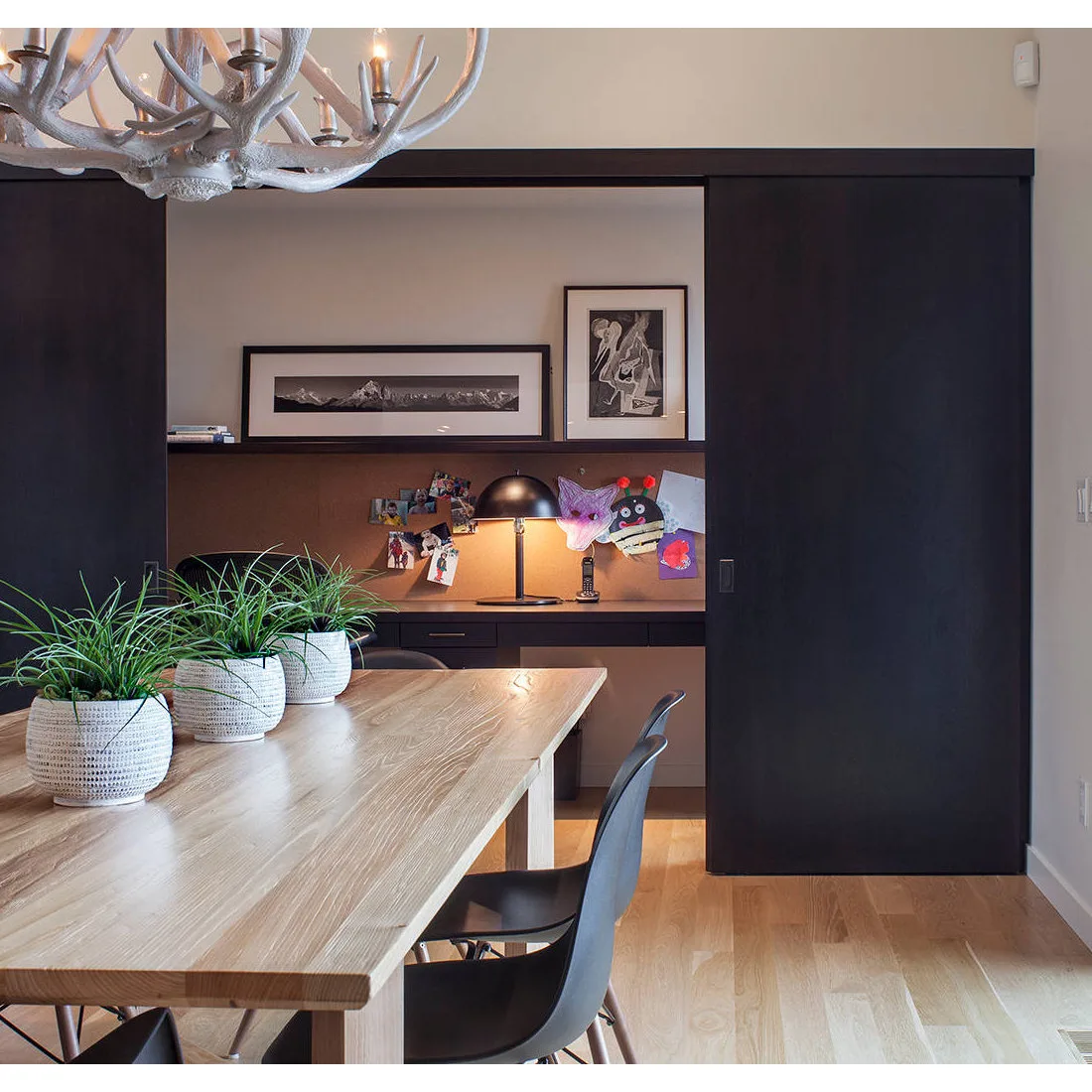 Dining table with black chairs in front of a recessed desk, corkboard and dark sliding doors