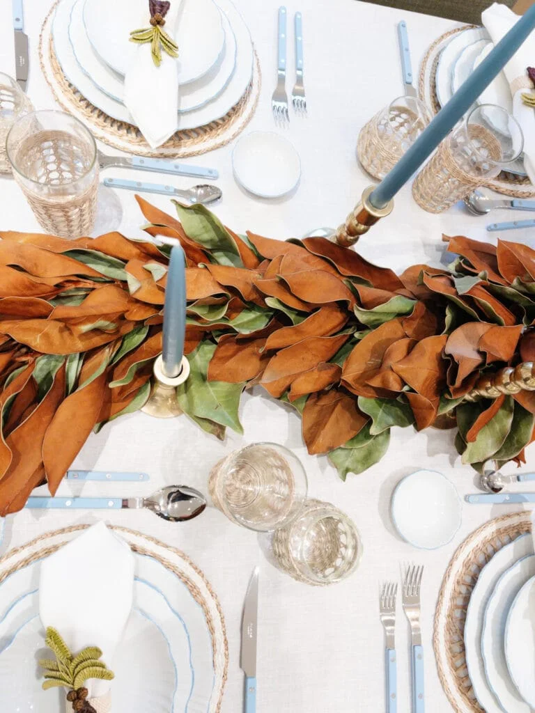 A palm-shaped beaded ornament rests on a white napkin over blue-edged plates and a woven charger beside blue-handled cutlery