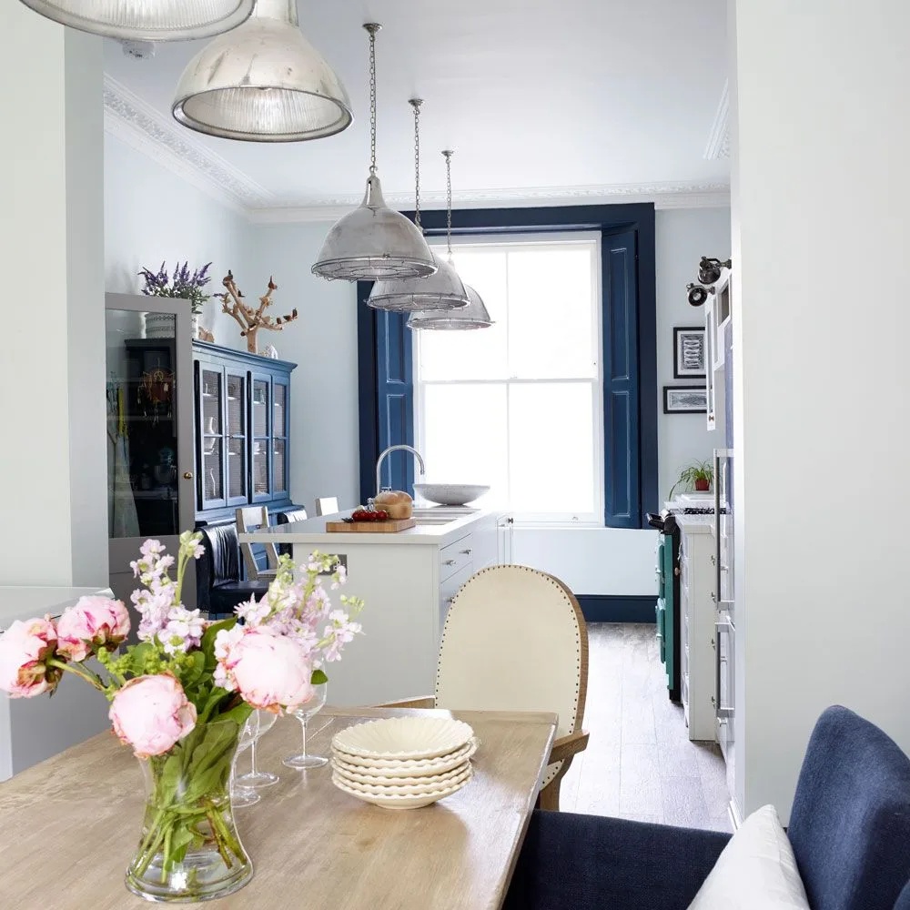 Metal pendant above a wood dining table with matching metal lights visible in the kitchen beyond