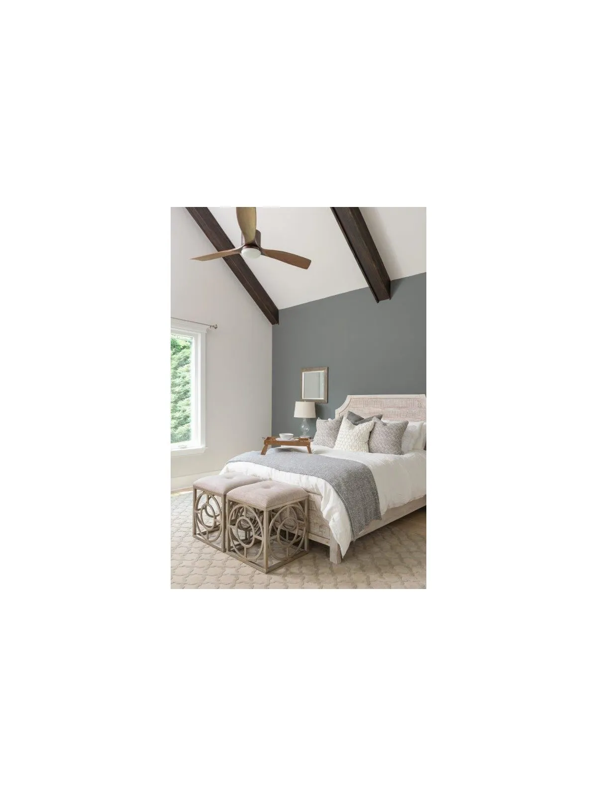 Dark ceiling beams cross a pale bedroom above a light upholstered bed.