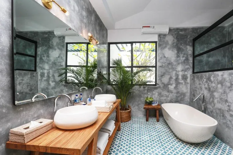 Mottled gray bathroom walls around a wood double-basin counter, leafy plant and blue-green patterned floor