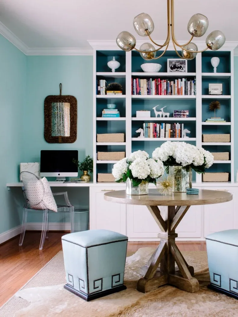 Aqua office with white shelving, a built-in computer desk and a gold-toned globe chandelier above a round table.
