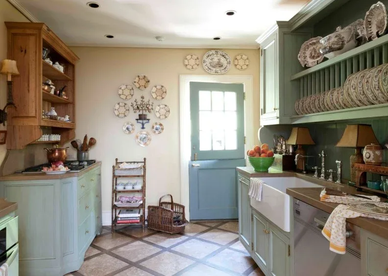 Green plate-rack cabinet and pale base cupboards opposite wood shelving, with wall-mounted dishes and a green glazed door