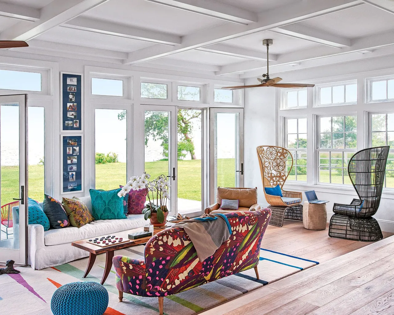 A pale sofa faces a colorful patterned loveseat, with tall open-backed chairs beside broad windows.