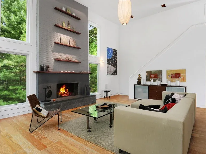 Tall gray brick fireplace between high windows with several narrow wooden display shelves above it.