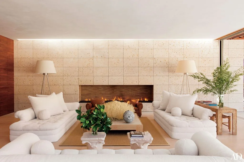 A long fireplace opening crosses a pale tiled wall behind low white sofas, a wooden table and matching floor lamps