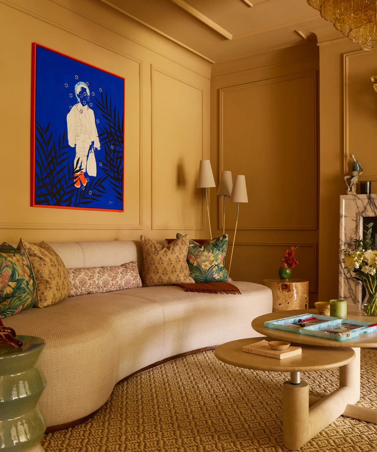 A curved cream sofa sits against mustard-colored walls beneath vivid artwork