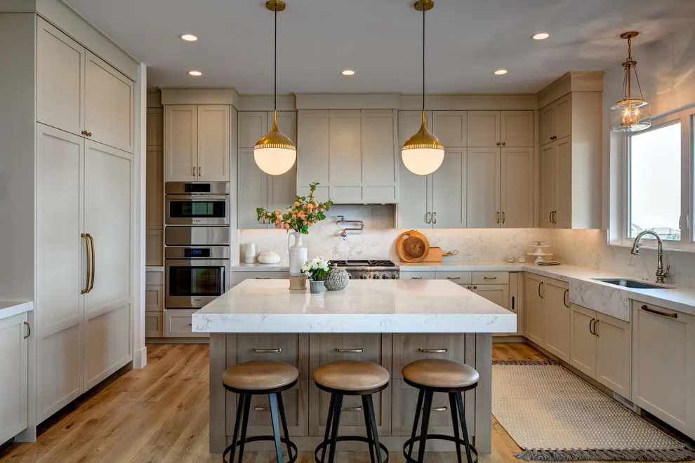 Warm beige cabinets sit behind a pale island beneath two rounded pendants