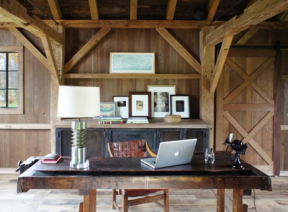A dark desk sits beneath exposed timber framing in a roof-level studio