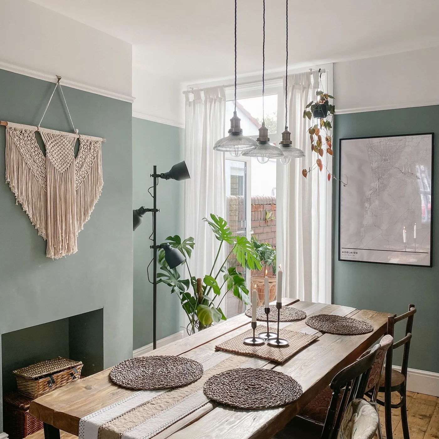 Three clear pendants over a wood table with a black multi-shade floor lamp in a green dining corner