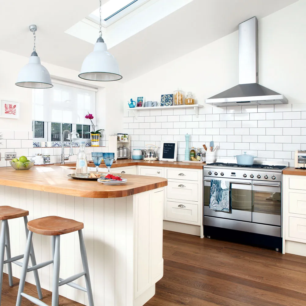 Cream-toned cabinets and a curved wooden breakfast counter sit beneath skylights and pale pendants