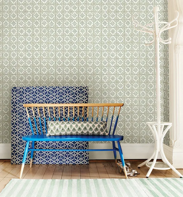 Blue spindle bench in front of a geometric panel and pale patterned wallpaper beside a coat stand