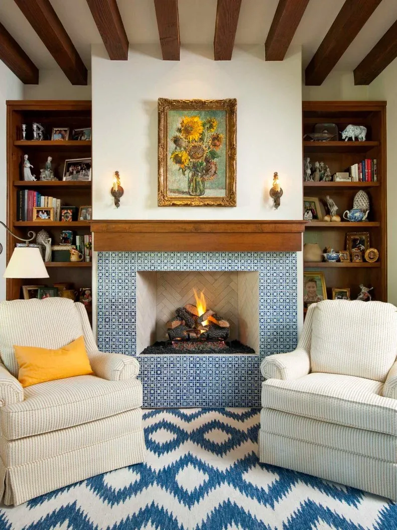Blue patterned tile fireplace with wood mantel, sunflower picture, side bookshelves and blue and white rug