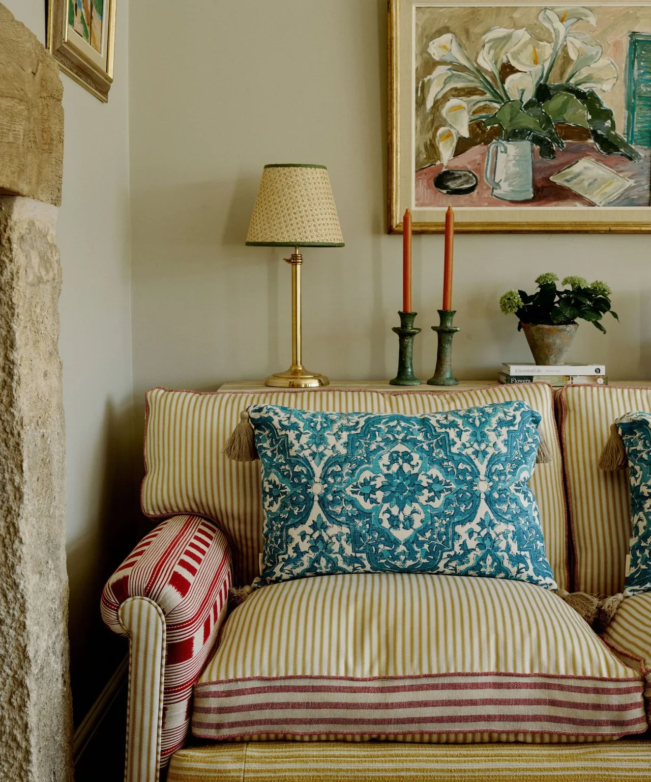 Teal patterned cushion on a chair with softly colored stripes beside a lamp and framed floral art